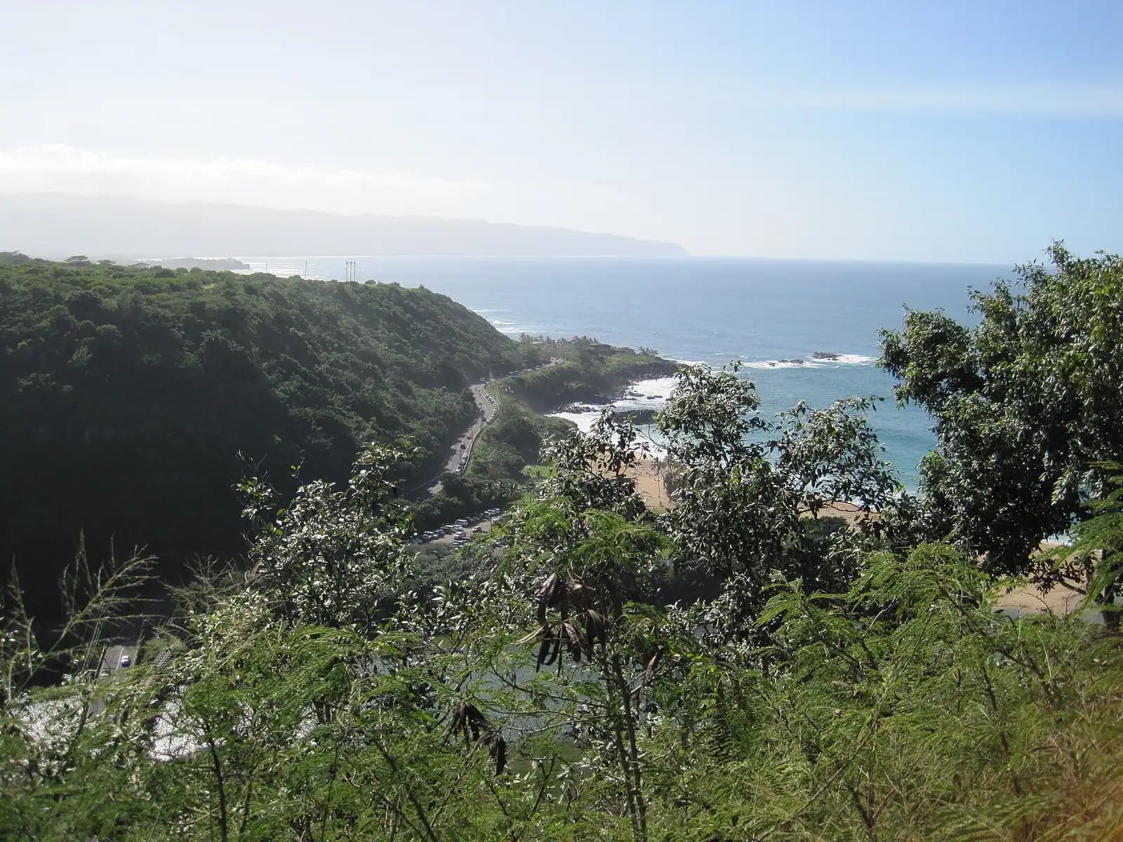A flat dirt track running along a dry rocky coastline with steep ridges rising inland