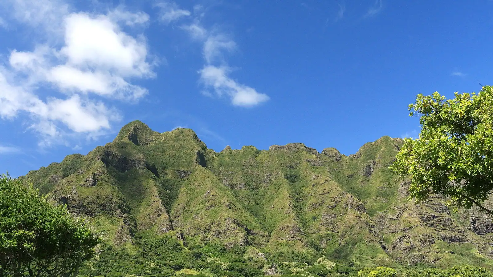 A wide green valley floor enclosed by steep fluted ridges under scattered cloud